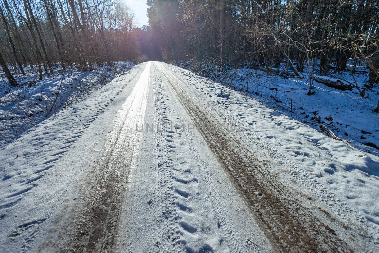 Snow-covered slippery road in the forest, sunny cold winter day