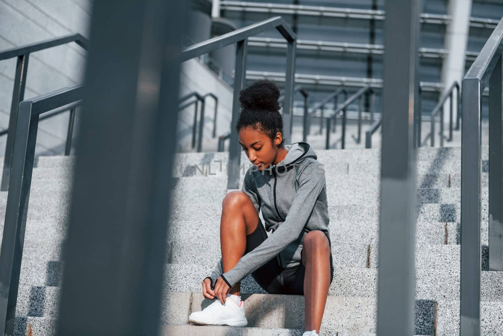 Sits on stairs. Young african american woman in sportive clothes have workout outdoors at daytime by Standret