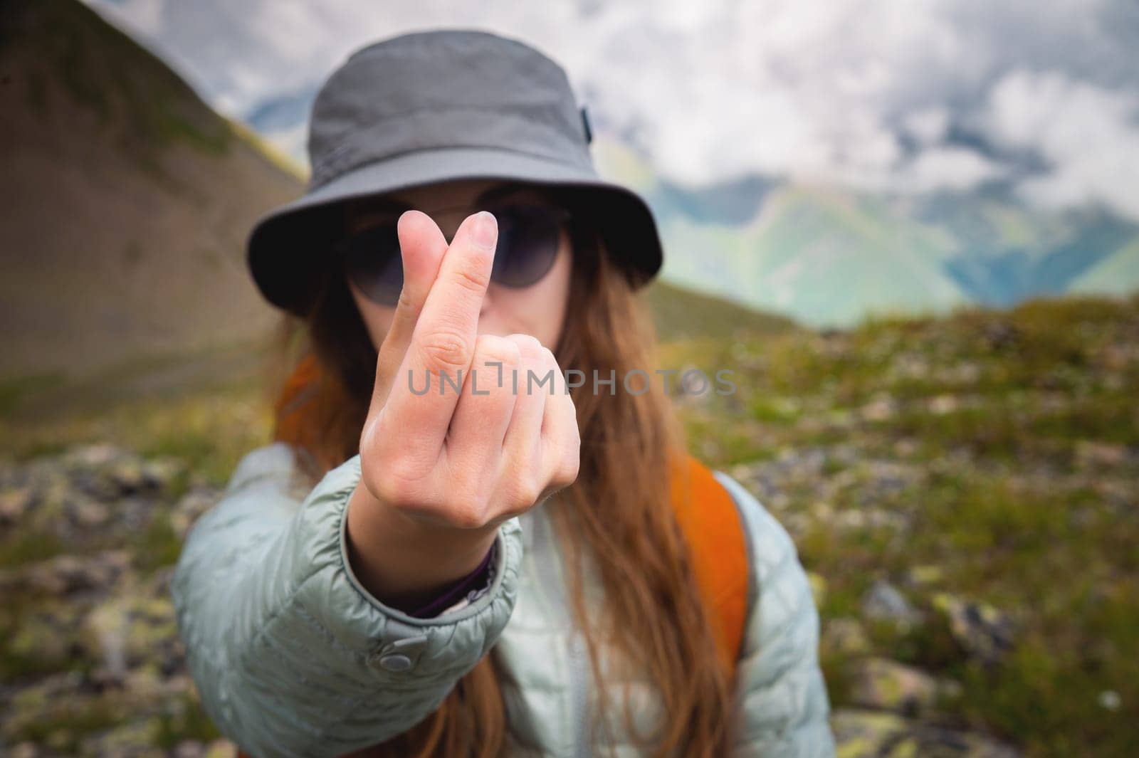 A cute girl shows a Korean heart sign with her fingers while standing against the backdrop of mountains. Close-up, love concept.