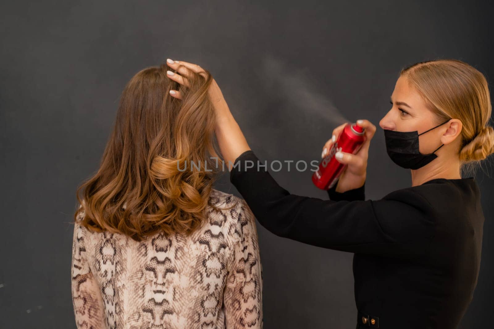 Women salon hairstyle. Hairdresser uses hairspray on client's hair in salon, Portrait of two beautiful women.