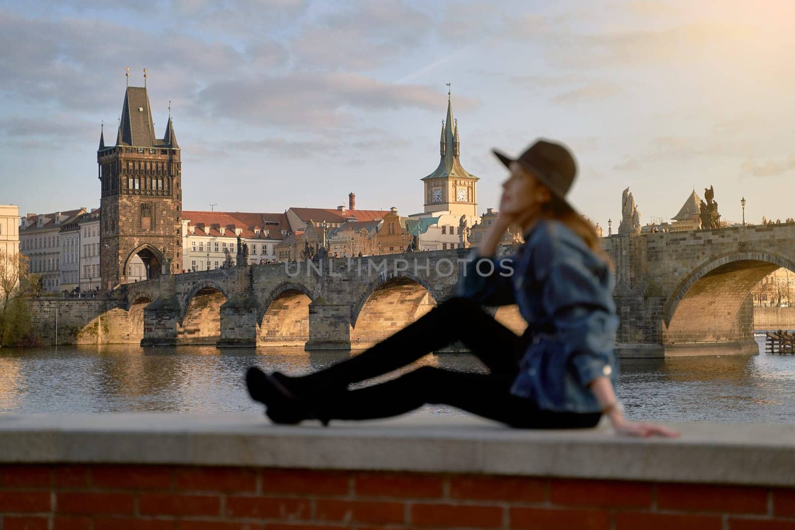 Stylish young beautiful woman earing black hat in Prague with Charles Bridge on background. Elegant retro lady fine art portrait.