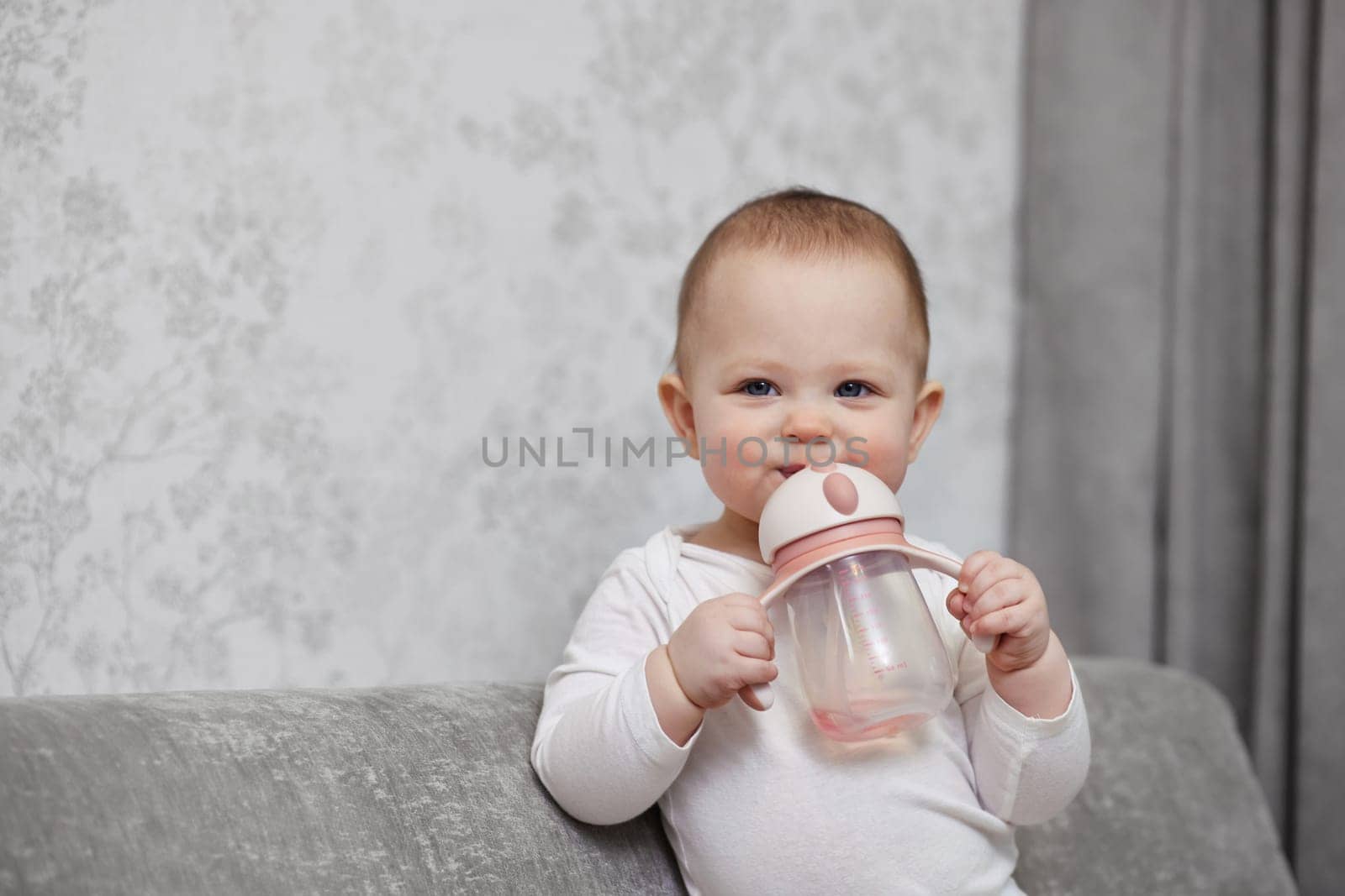 little child girl holding bottle and drinking water at home.
