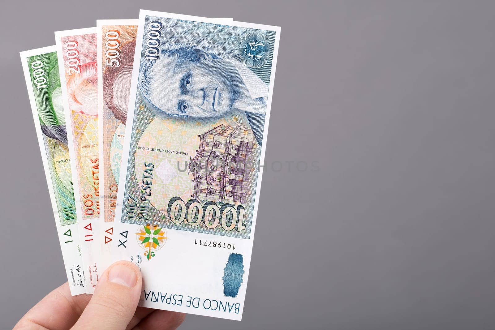 Spanish money - Peseta in the hand on a gray background