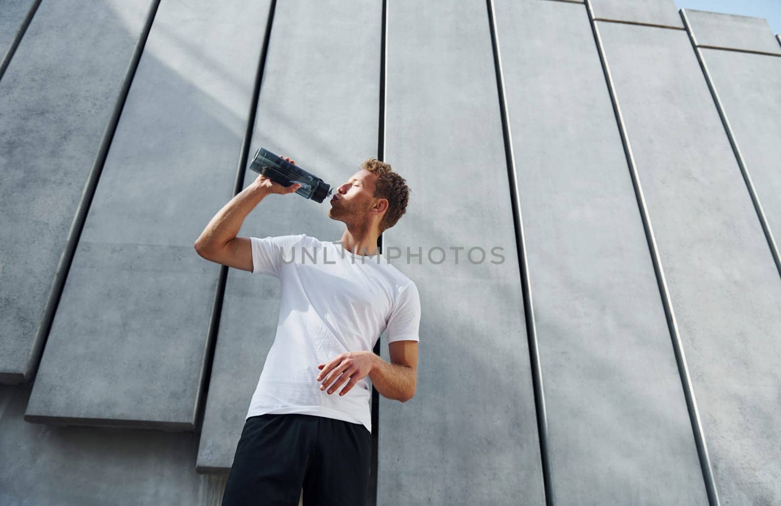 Against building exterior. Young man in sportive clothes have workout outdoors at daytime.