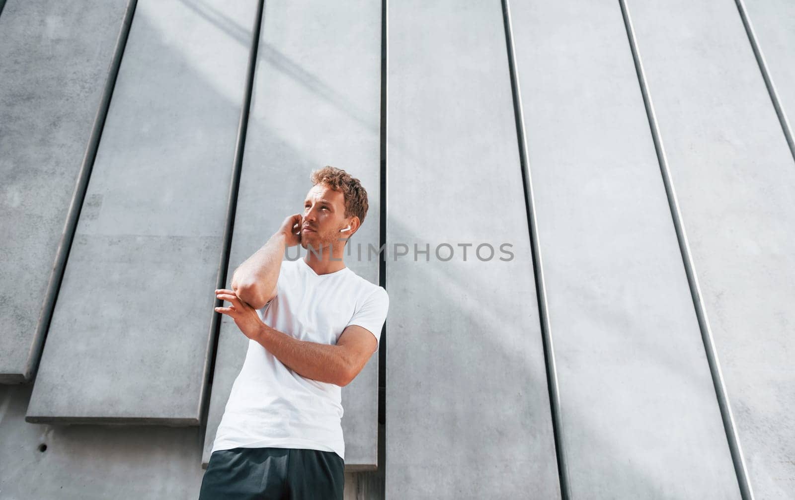 Takes a break. Young man in sportive clothes have workout outdoors at daytime.