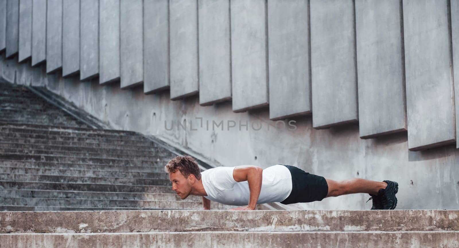 Against building exterior. Young man in sportive clothes have workout outdoors at daytime.