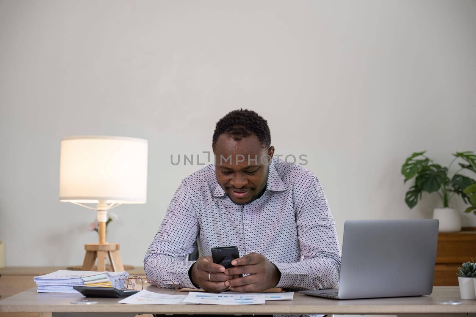 Business man using mobile smart phone, busy working on laptop computer browsing internet or checking internet application on smartphone with financial data on office desk.