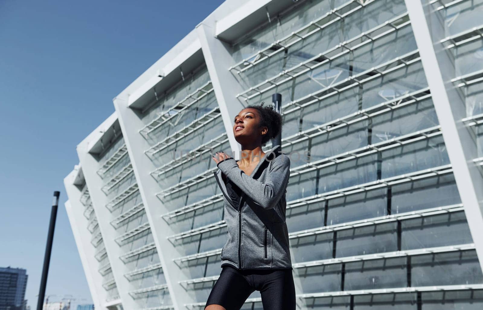 Big building behind. Young african american woman in sportive clothes have workout outdoors at daytime.