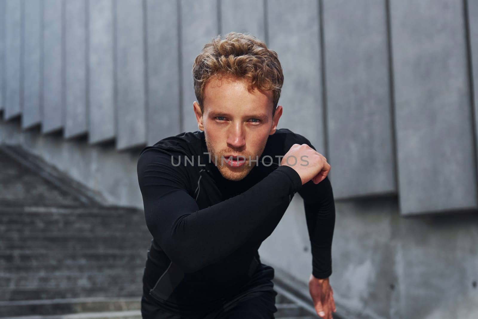 Runs forward. Young man in sportive clothes have workout outdoors at daytime.