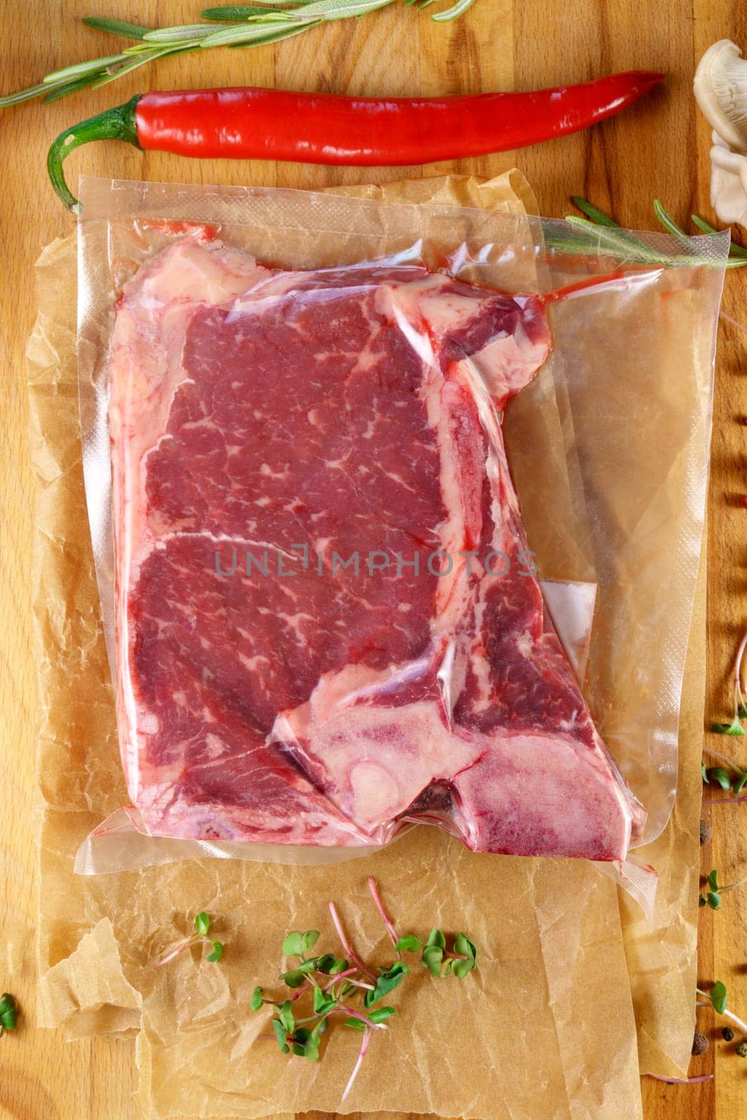 Raw meat in vacuum packaging on a wooden board with spices. Top view. Vertical photo