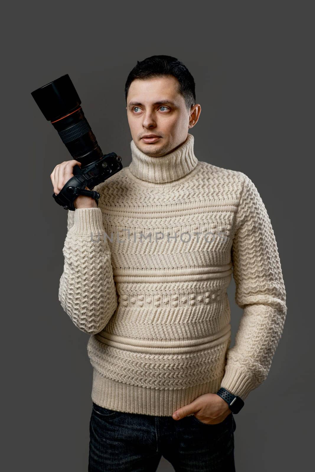 Professional young handsome photographer in sweater with digital camera isolated on gray background