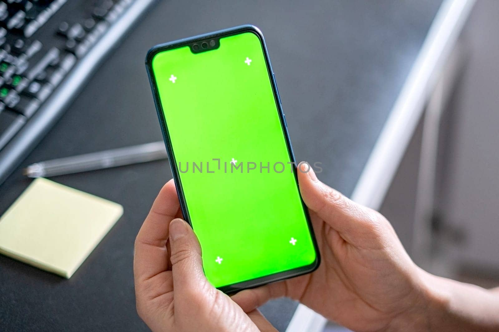 Woman hands hold a smartphone with green screen of workspace background. Chroma key phone. Successful sales strategy.