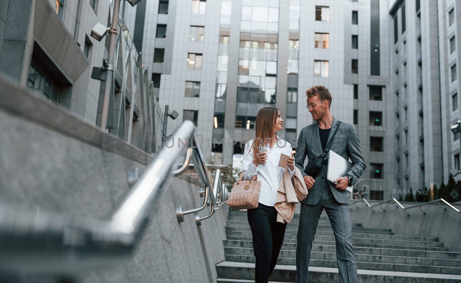 Closed laptop in hands. Woman and man in the town at daytime. Well dressed people by Standret