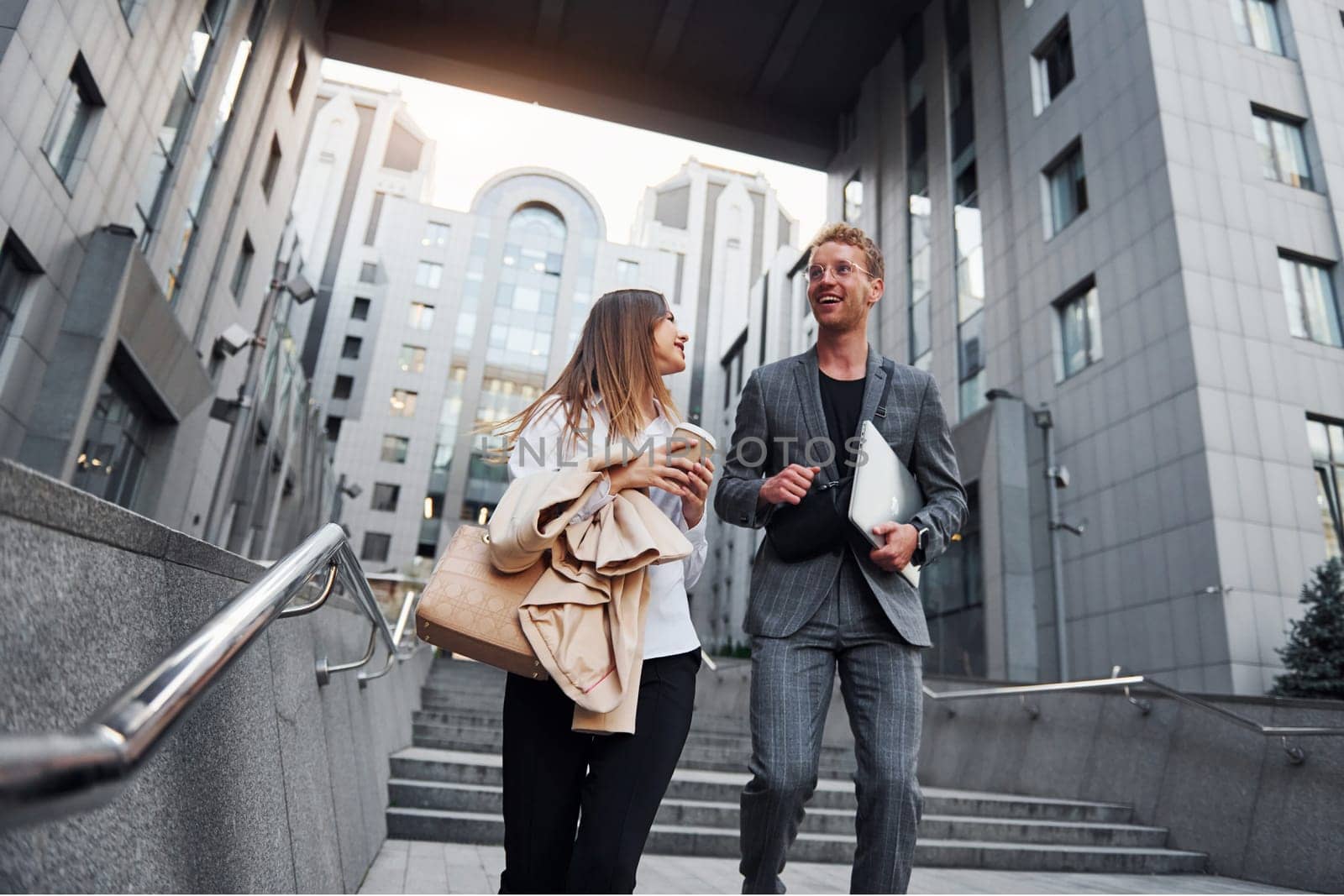 Closed laptop in hands. Woman and man in the town at daytime. Well dressed people by Standret