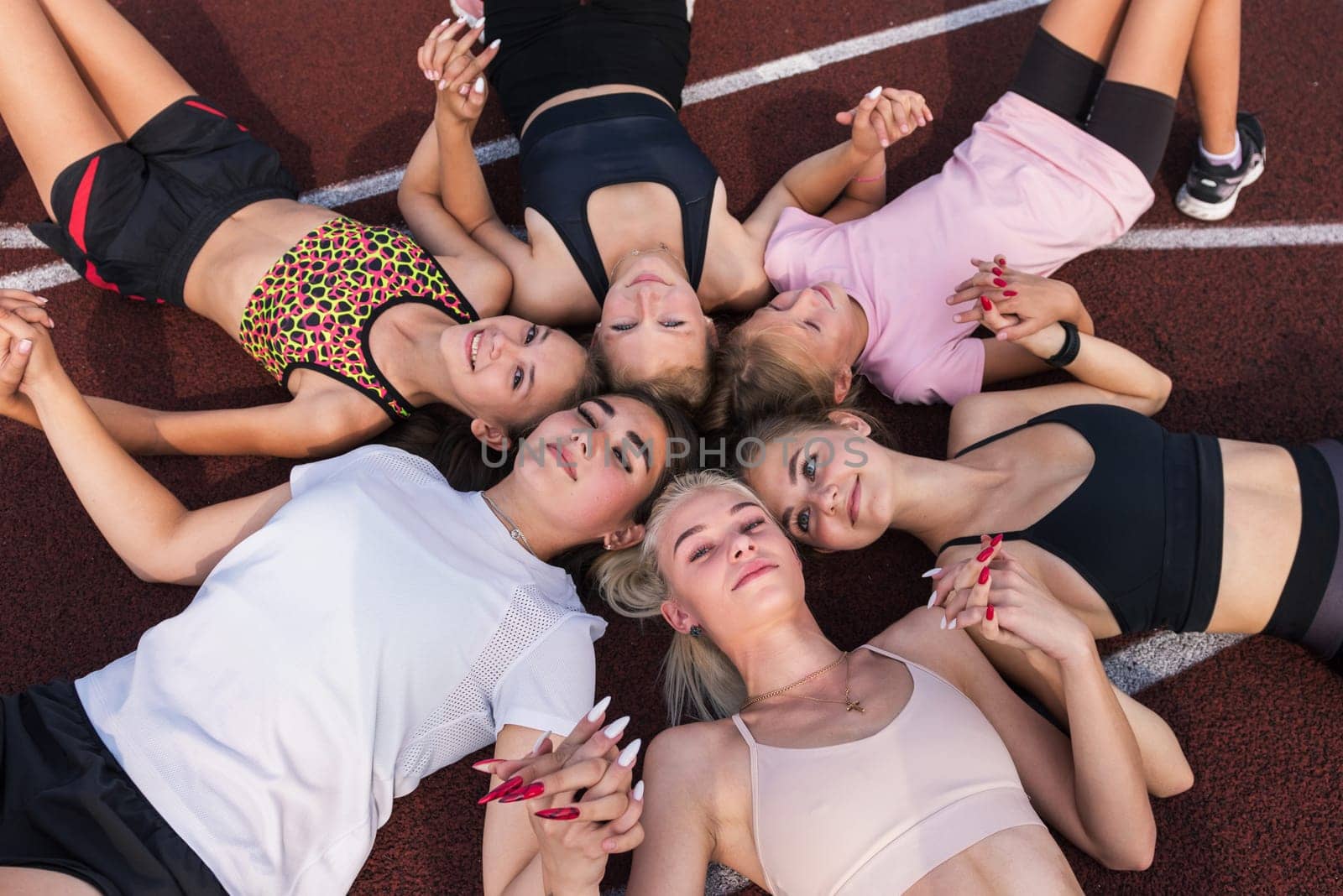 Group of tired and happy fit young girls resting on floor at stadium