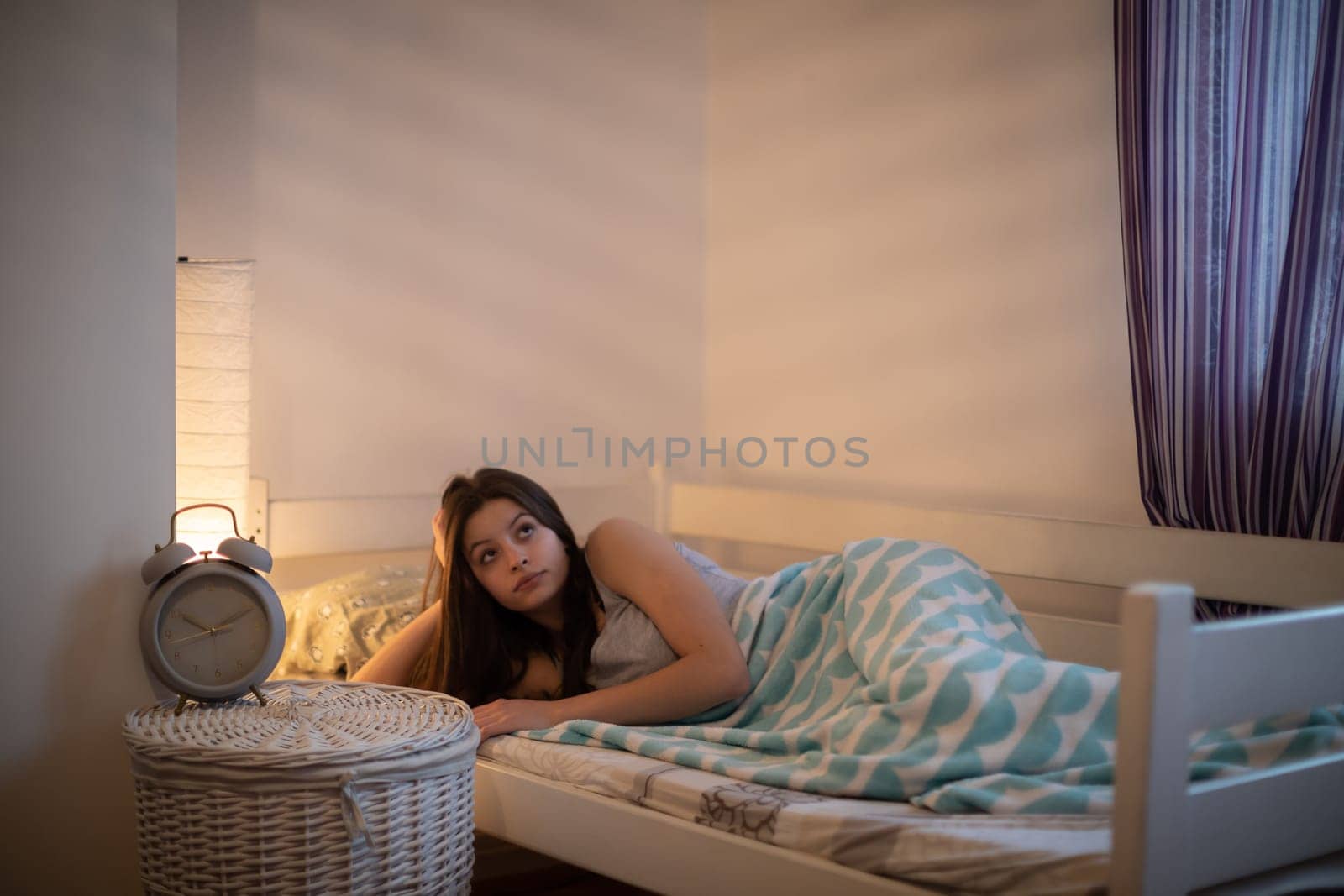 The girl lies under a blanket on the bed and rests. Bedroom in bright colors.