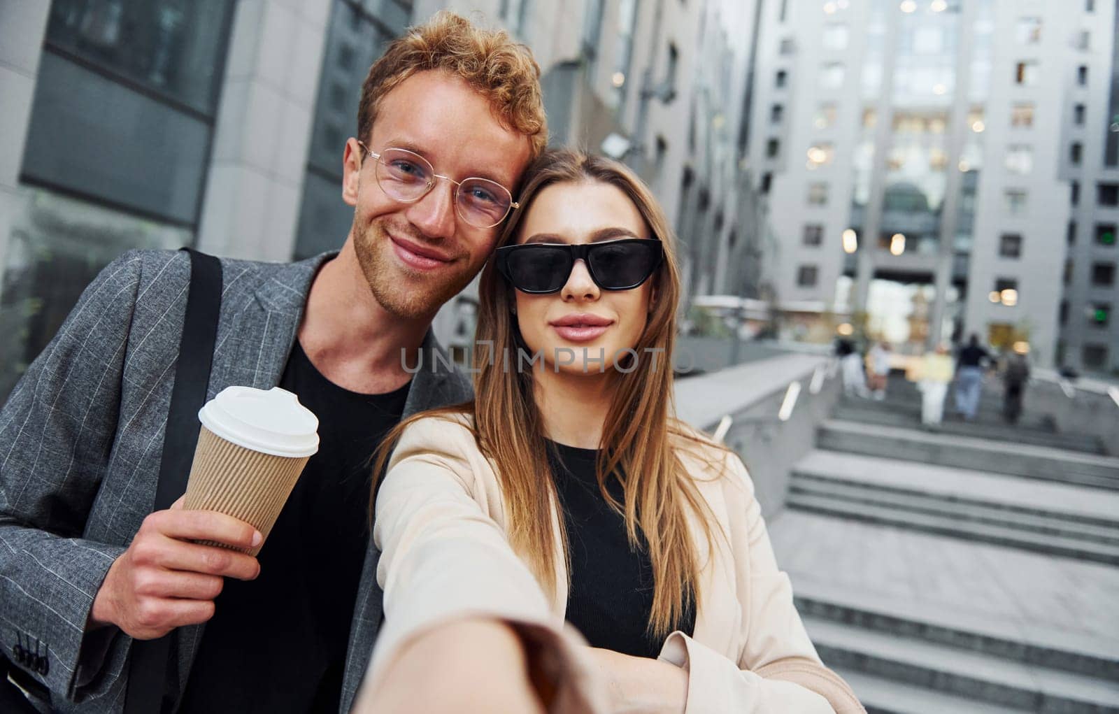 Makes selfie. Woman and man in the town at daytime. Well dressed people.