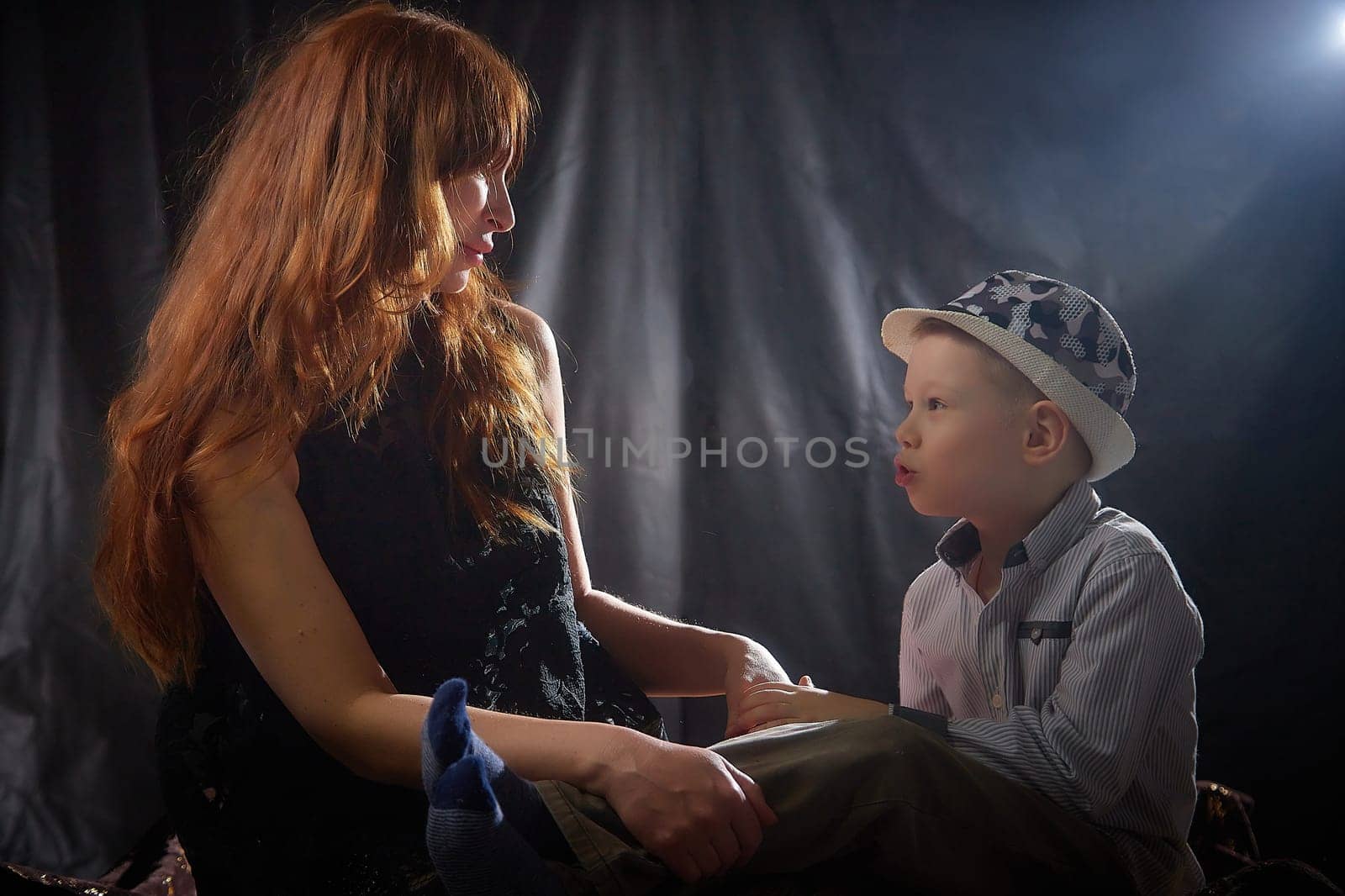 Woman with a boy in hat. Mom with son on a dark background. Family portrait with mother with red hair and boy having fun together by keleny