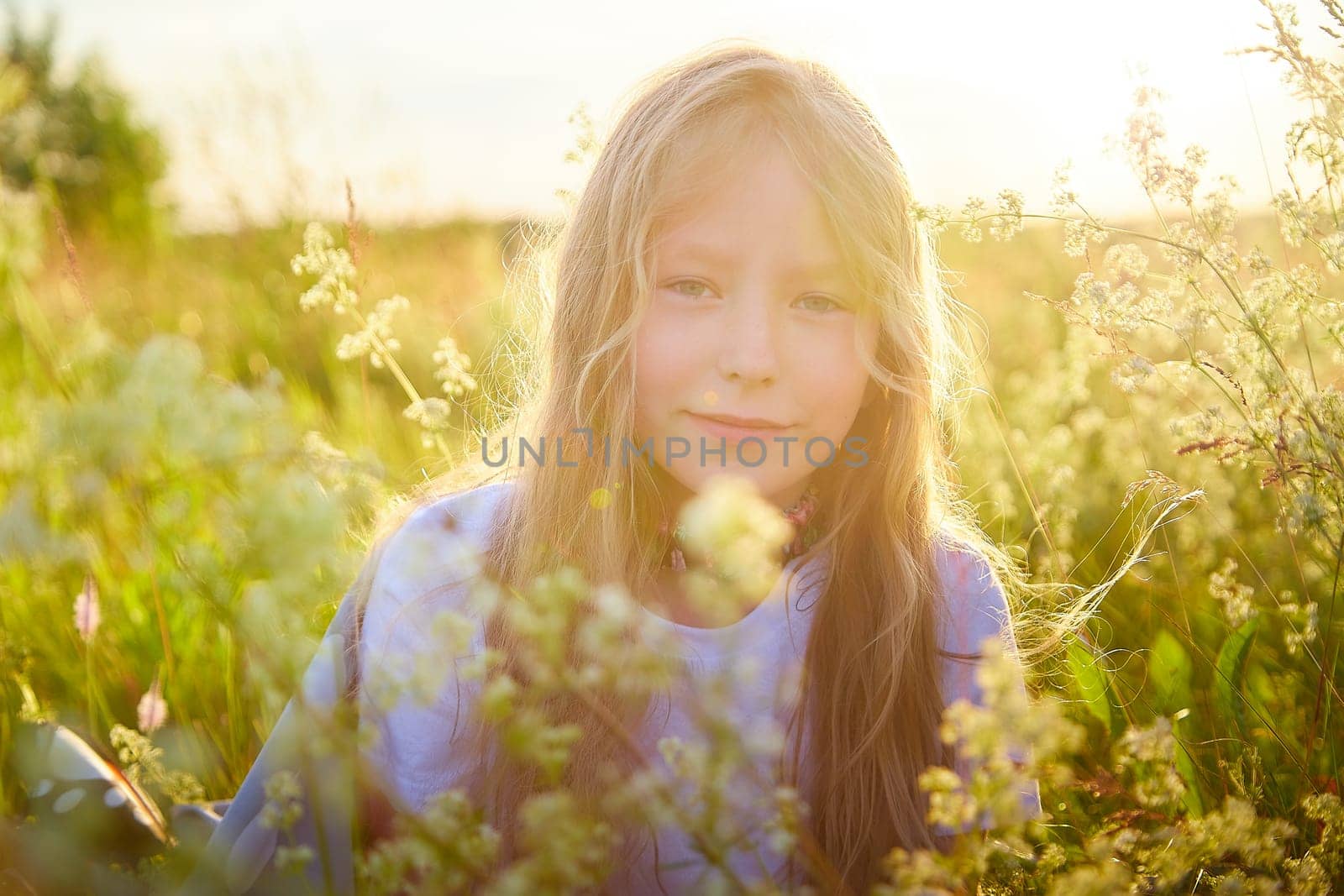 Portrait of pretty blonde girl having fun in a meadow on a natural landscape with grass and flowers on a sunny summer day. Portrait of a teenage child in summer or spring outdoors on field by keleny