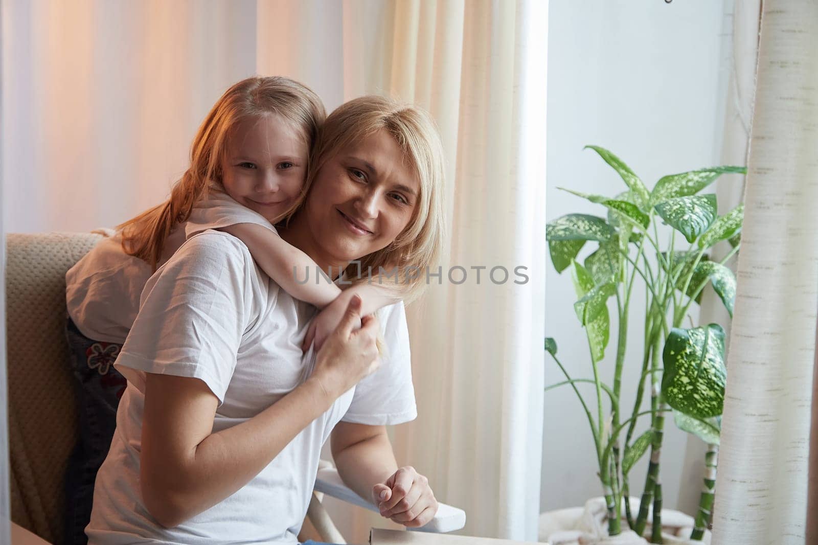 Happy loving family with mother and daughter having hugs in living room. Woman mom and small child girl inside of the home by keleny