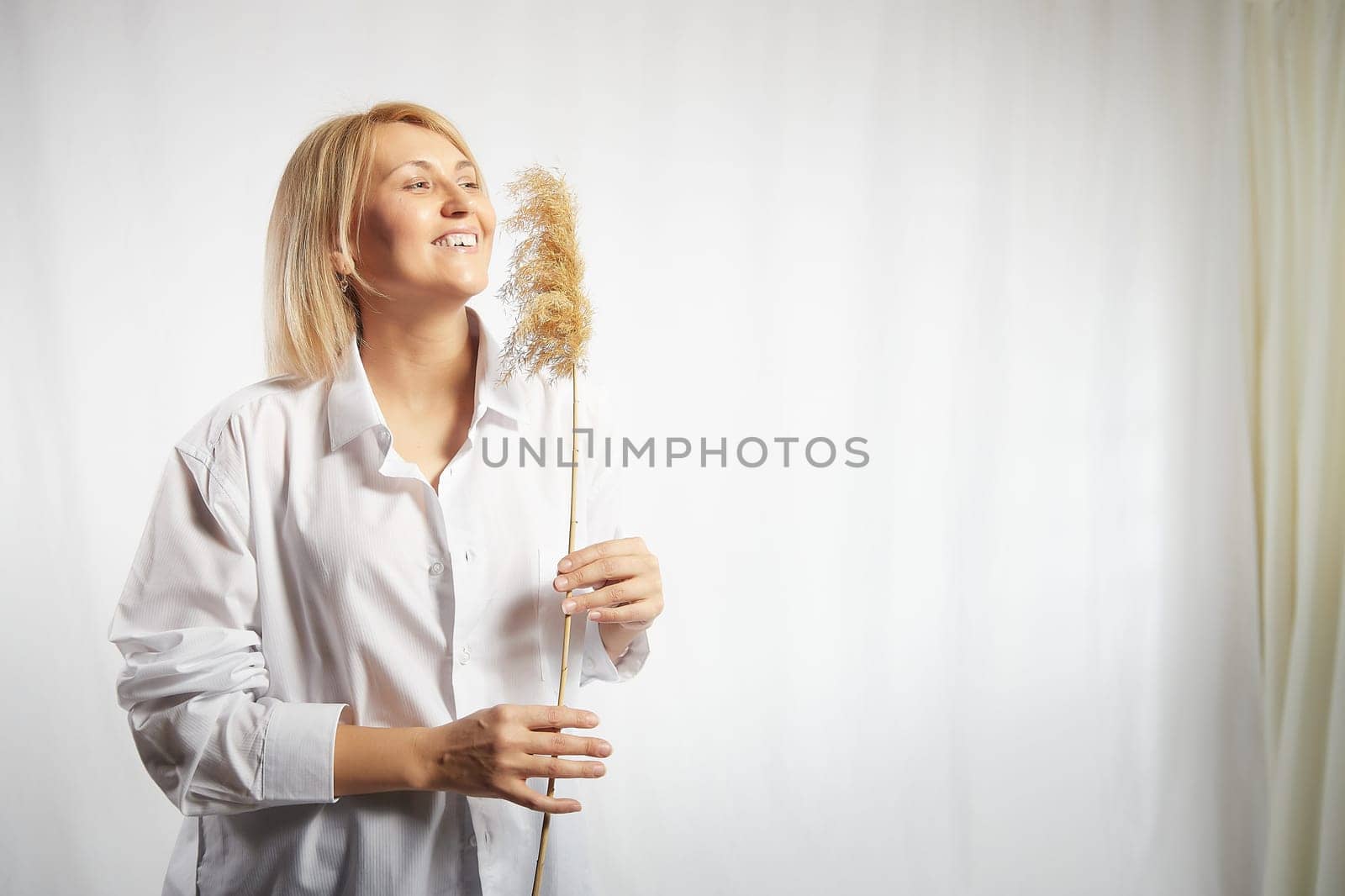 Portrait of a pretty blonde smiling woman with soft ear in hands posing on a white background. Happy girl model in white shirt in studio. The concept of softness, tenderness and dreams. Copy space