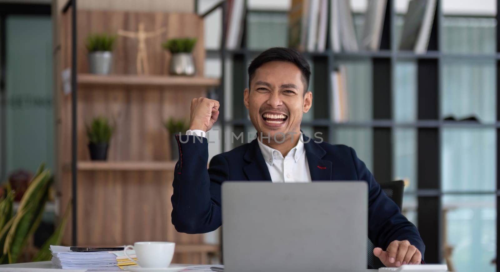 Happy young businessman looking at laptop computer in office, Excited asian man working at his workplace at modern co-working, successful people..