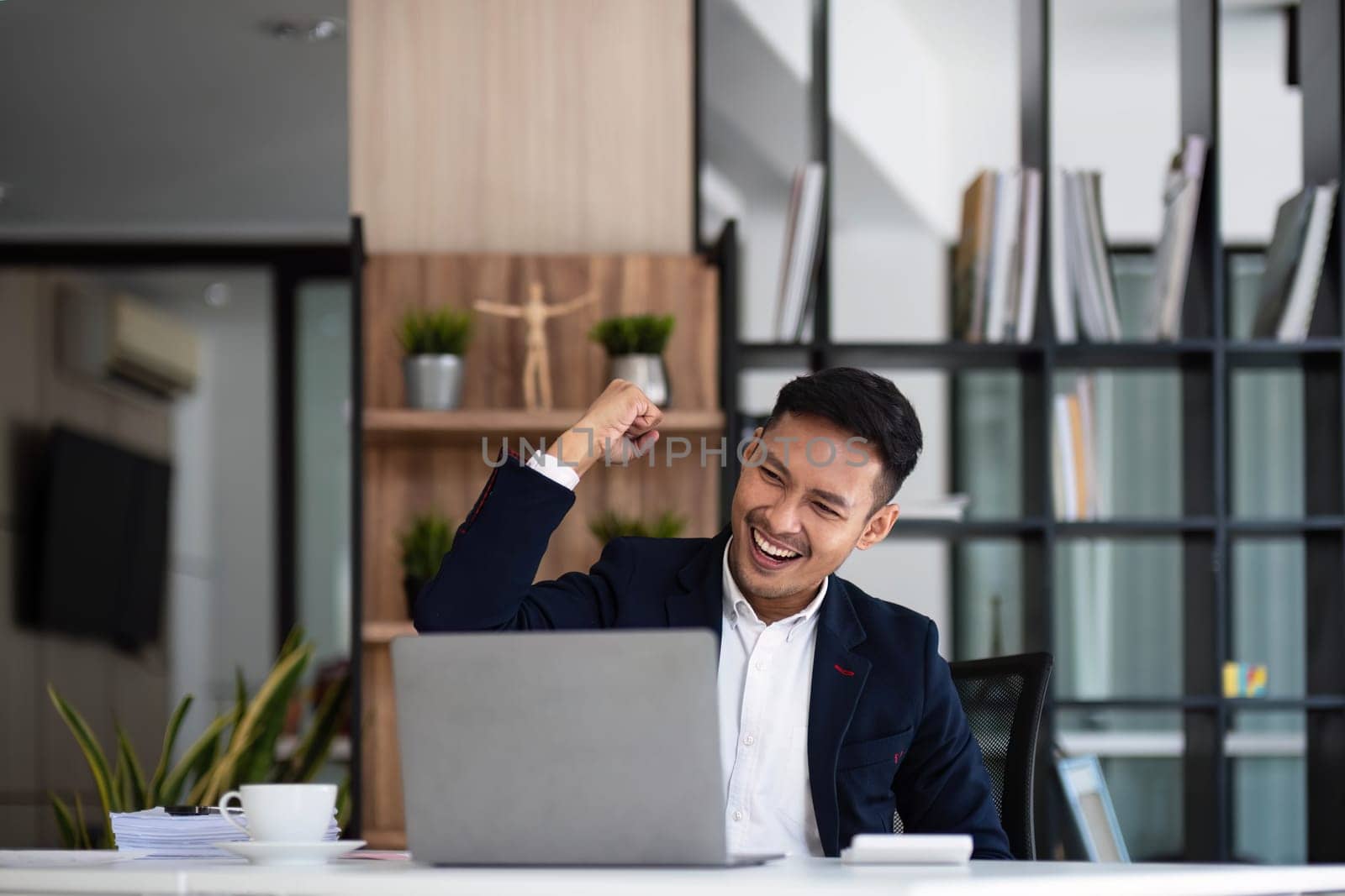 Happy young businessman looking at laptop computer in office, Excited asian man working at his workplace at modern co-working, successful people by wichayada