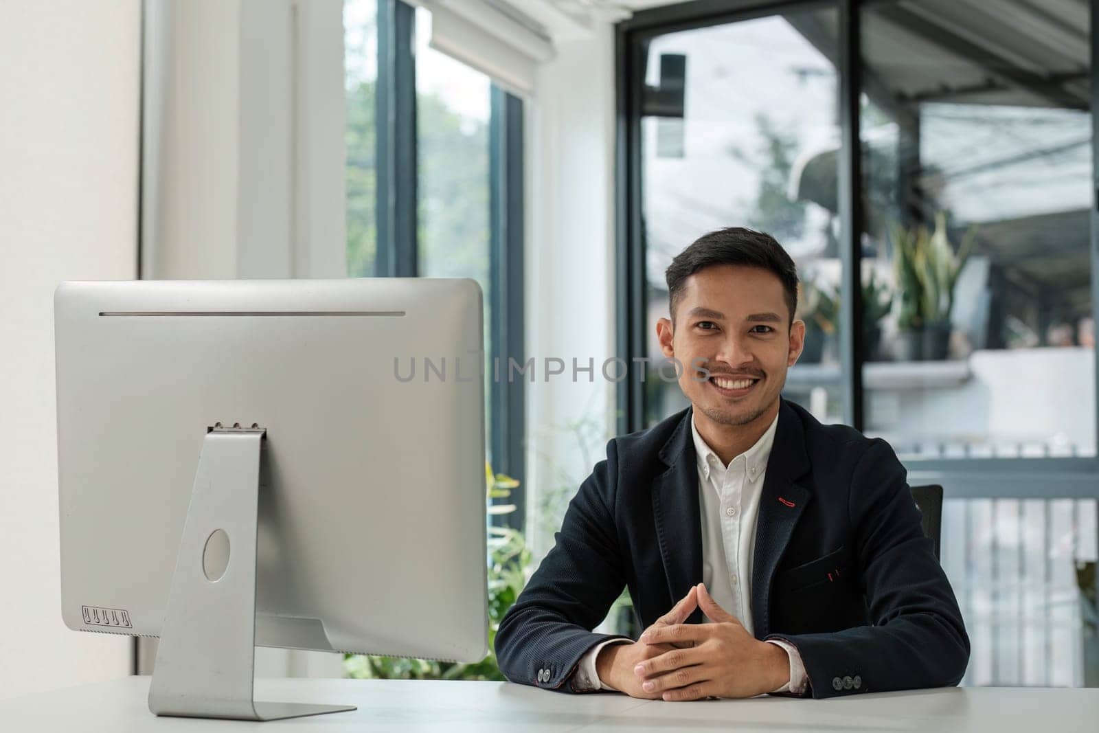 Asian business man wears a black suit and sitting in office and typing to keyboard on laptop and smiling confidently...