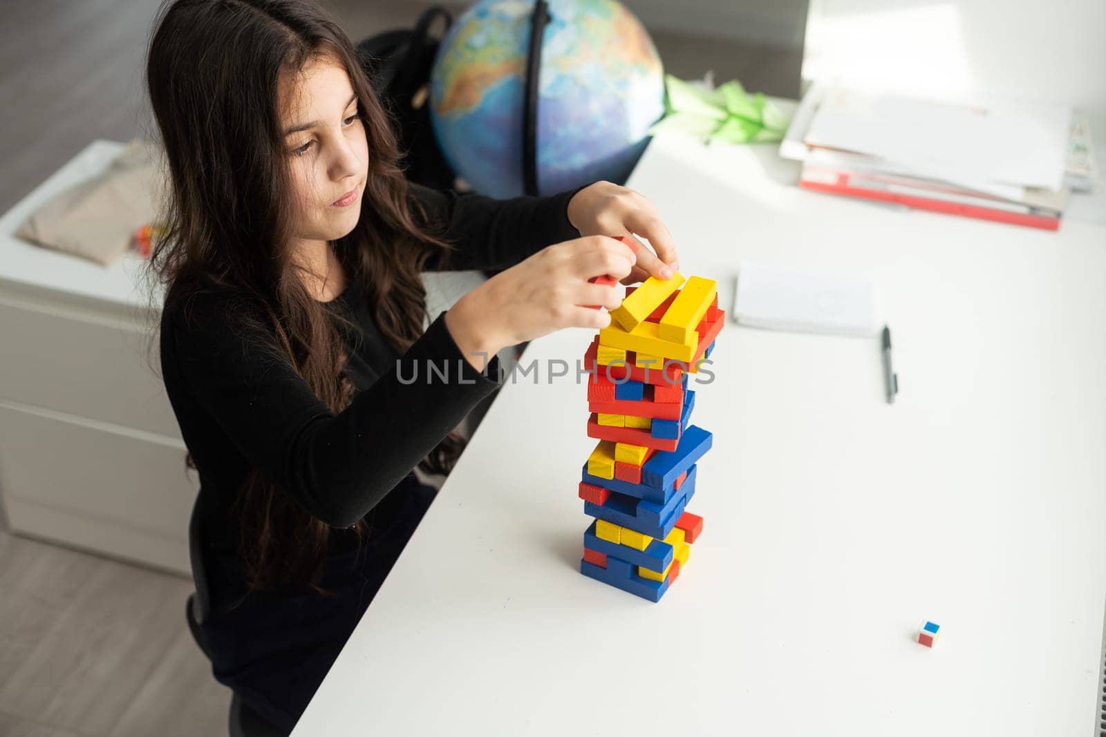 a little happy girl is playing the board game jenga at the table. Construction of a tower made of wooden cubes by Andelov13