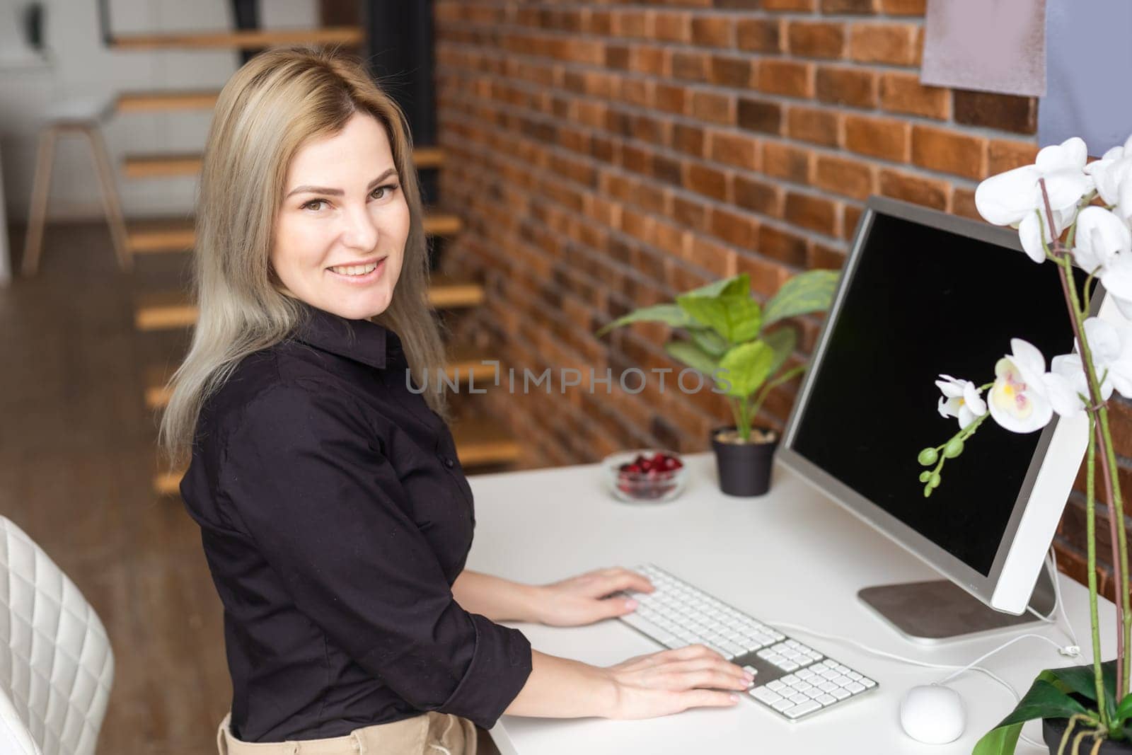 Successful female grapic designer watching tutorial about creative ideas at computer during working process in office. Positive student with blonde hair reading business news.