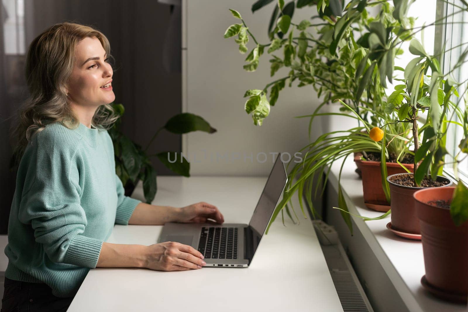 Young smiling happy satisfied employee business woman in casual blue shirt hold pen sit work at workplace white desk with laptop pc computer at light modern office indoors. Achievement career concept. by Andelov13