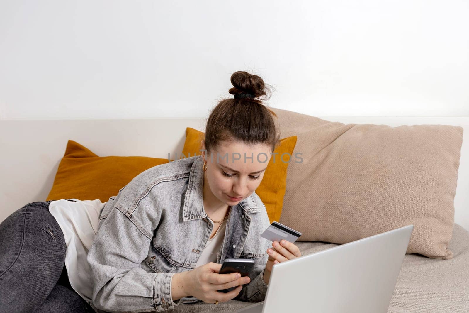 Young brunette woman smiling while surfing the web on her laptop and holding credit card in her hand trying to buy something online. Easy online shopping at home, e-commerce. Cosy interior