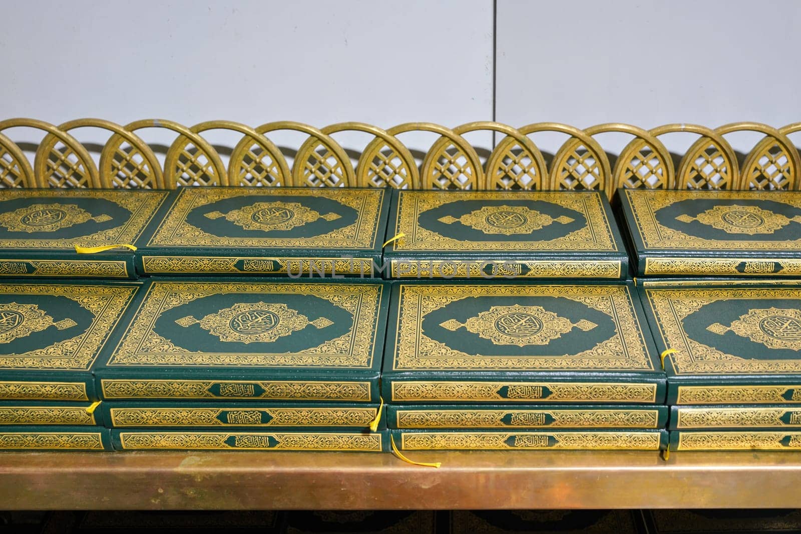 Stacks of green and golden Quran or Quraan books at shelf, closeup detail.