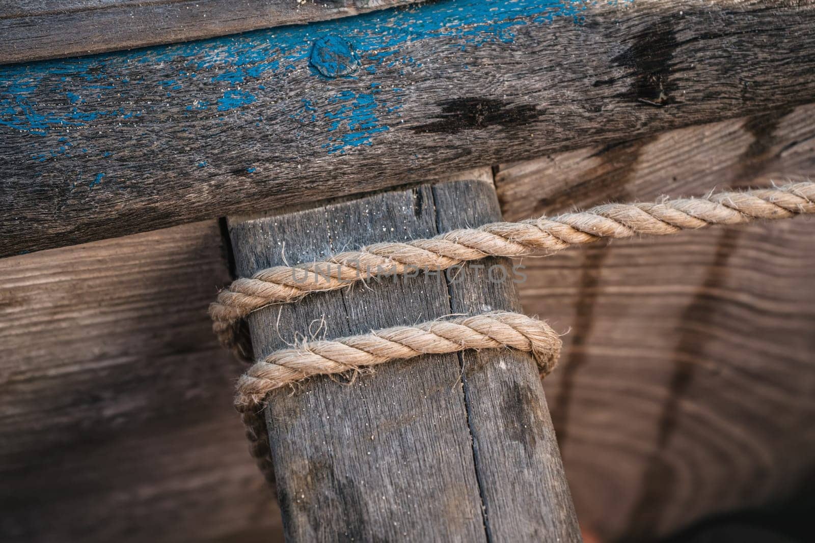 Simple natural rope tied around wooden part of fishing boat, closeup detail.