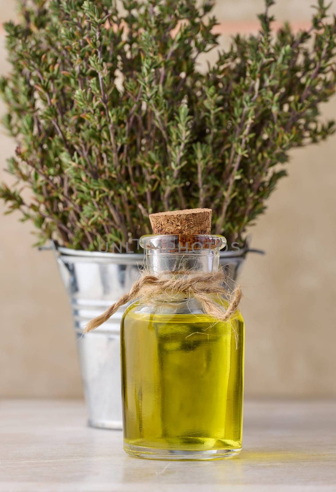 A clear glass bottle with oil and fresh thyme branches in a miniature bucket on a wooden table, cosmetic procedure oil by ndanko