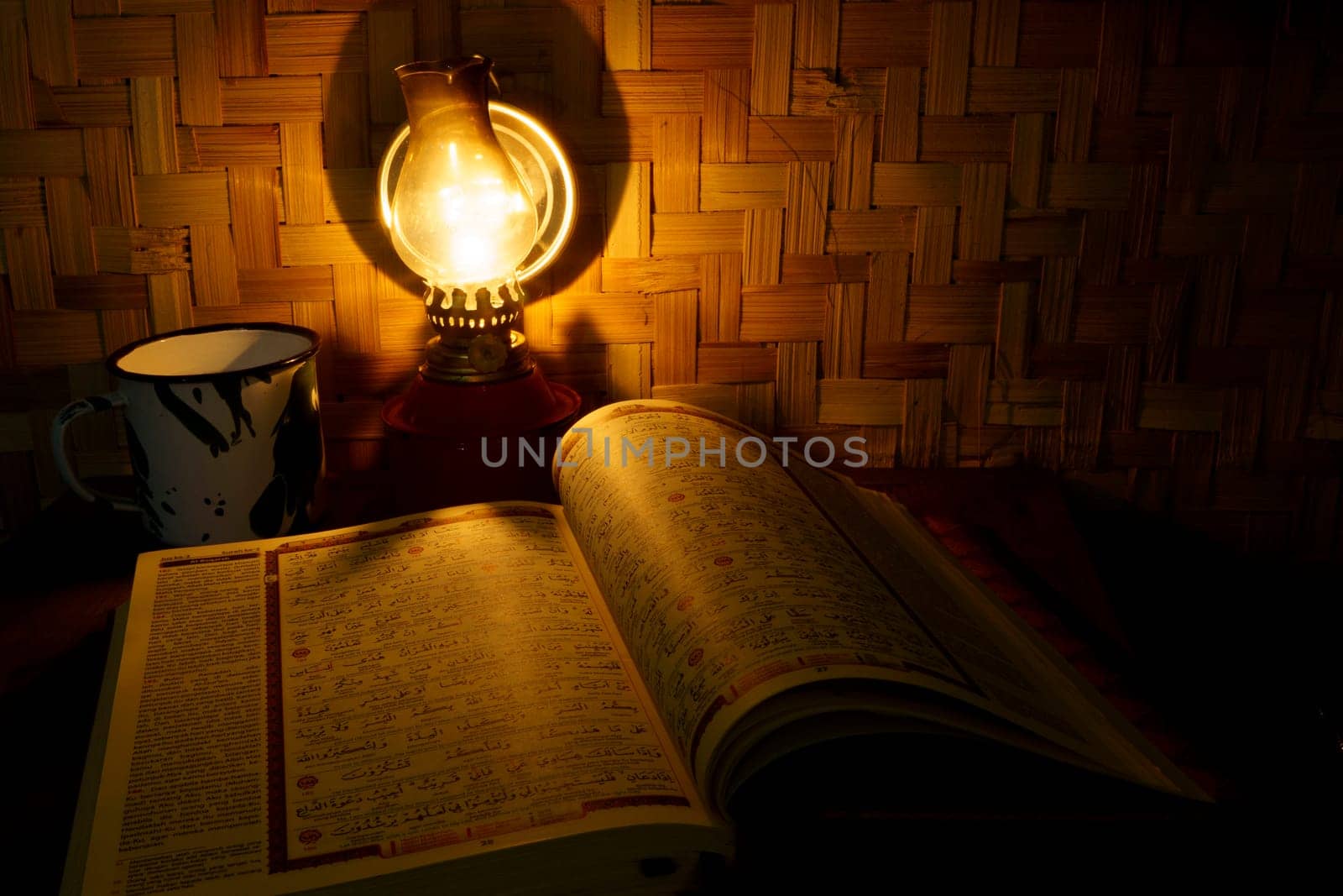 Holy Quran on the wooden table with vintage traditional kerosene lamp and woven bamboo as background. Studio shot with long exposure. Defocused.