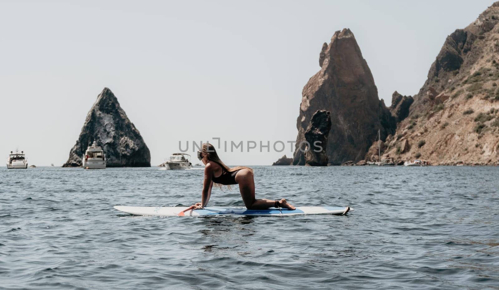 Close up shot of beautiful young caucasian woman with black hair and freckles looking at camera and smiling. Cute woman portrait in a pink bikini posing on a volcanic rock high above the sea