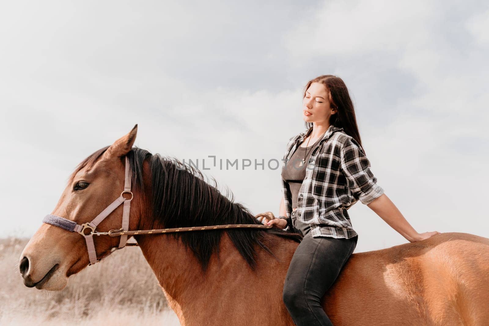 Cute happy young woman with horse. Rider female drives her horse in nature on evening sunset light background. Concept of outdoor riding, sports and recreation.