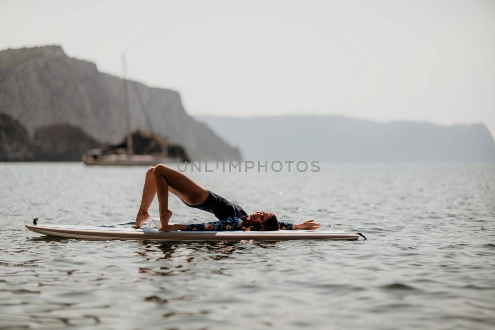 Woman sup yoga. Middle age sporty woman practising yoga pilates on paddle sup surfboard. Female stretching doing workout on sea water. Modern individual hipster outdoor summer sport activity