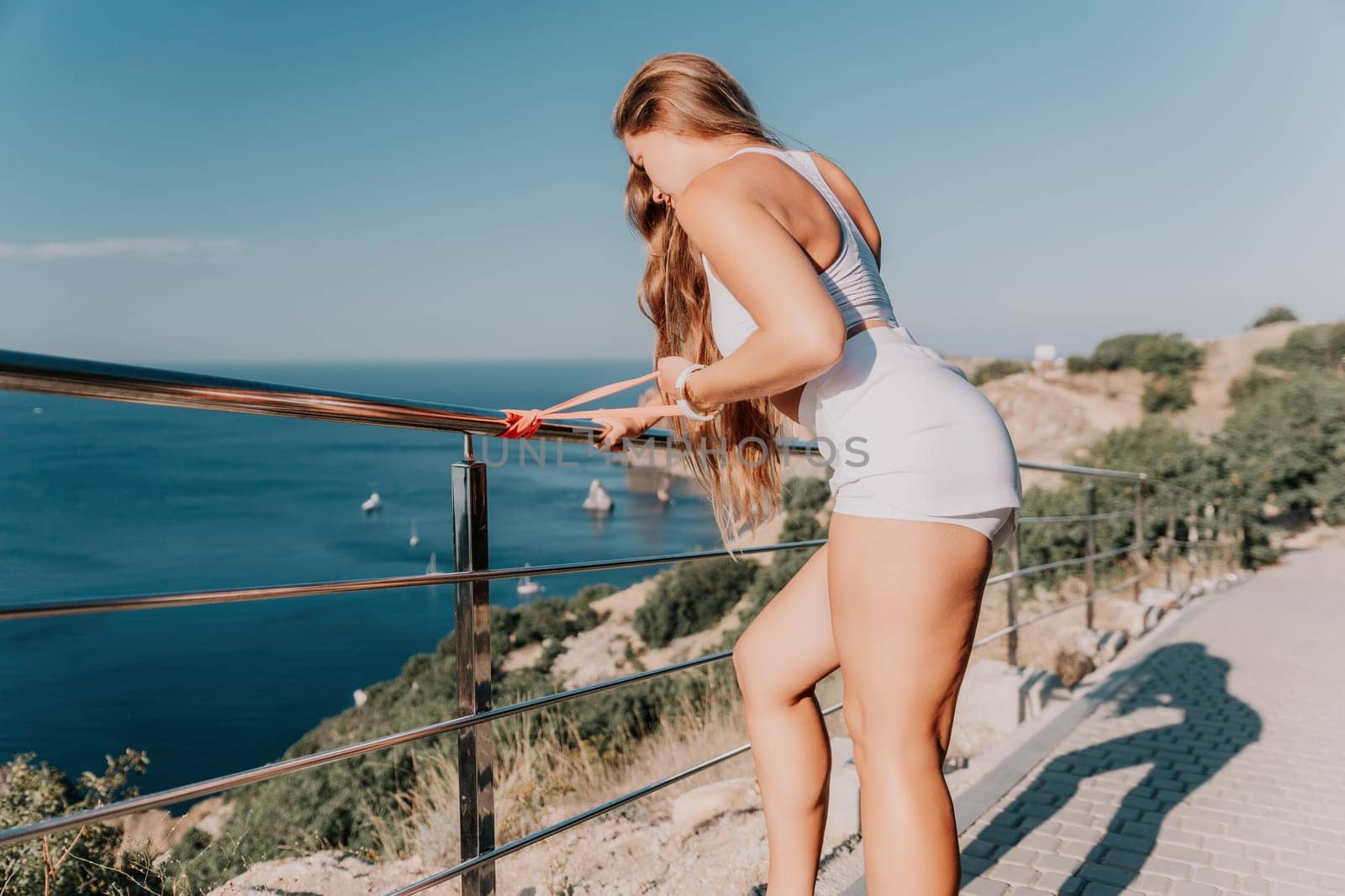 Fitness woman sea. Outdoor workout with fitness rubber bands in park over beach. Female fitness yoga routine concept. Healthy lifestyle. Happy fit woman exercising with rubber band in park