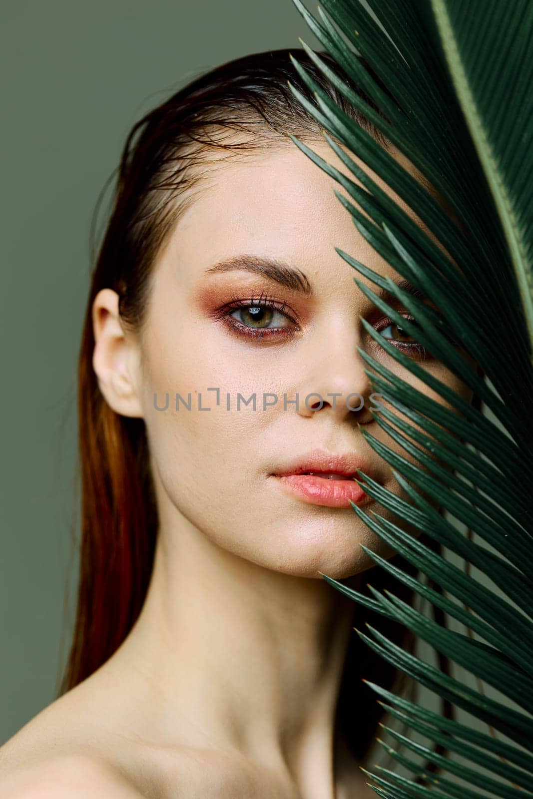 a close beauty portrait of a beautiful woman standing holding a tropical palm leaf in her hand, bringing it to her face, looking into the camera. Vertical photo without retouching of problem skin. High quality photo