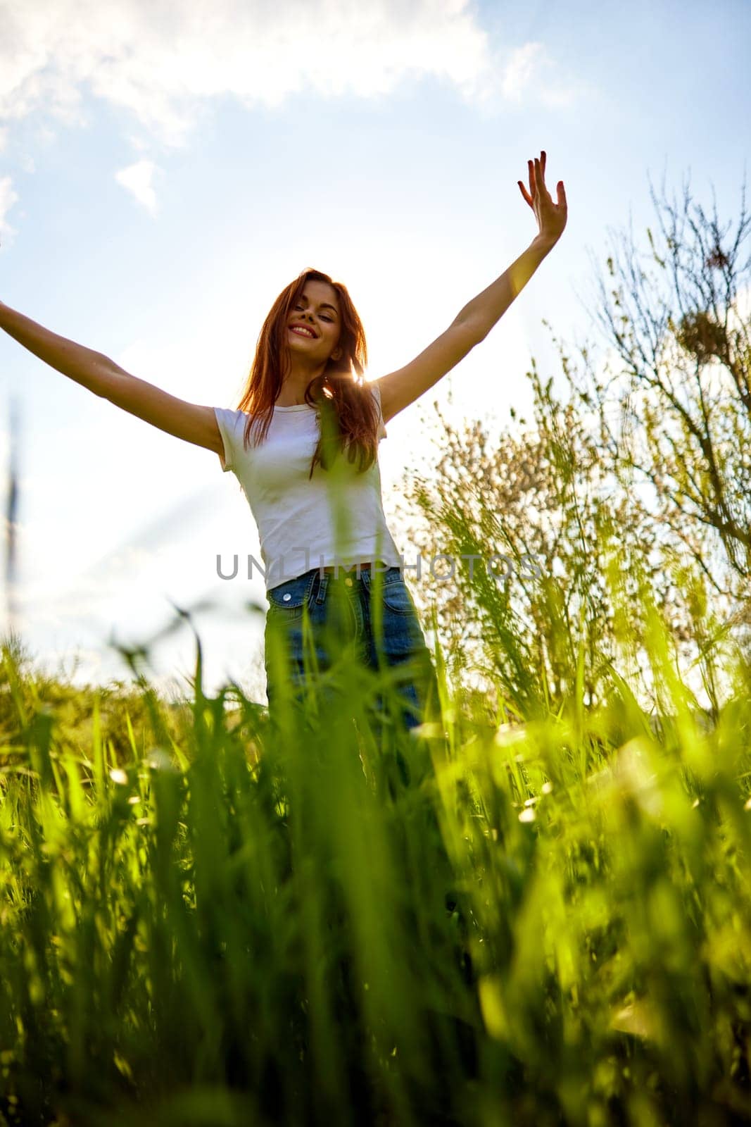 joyful slender woman posing in a field with her arms raised high. High quality photo