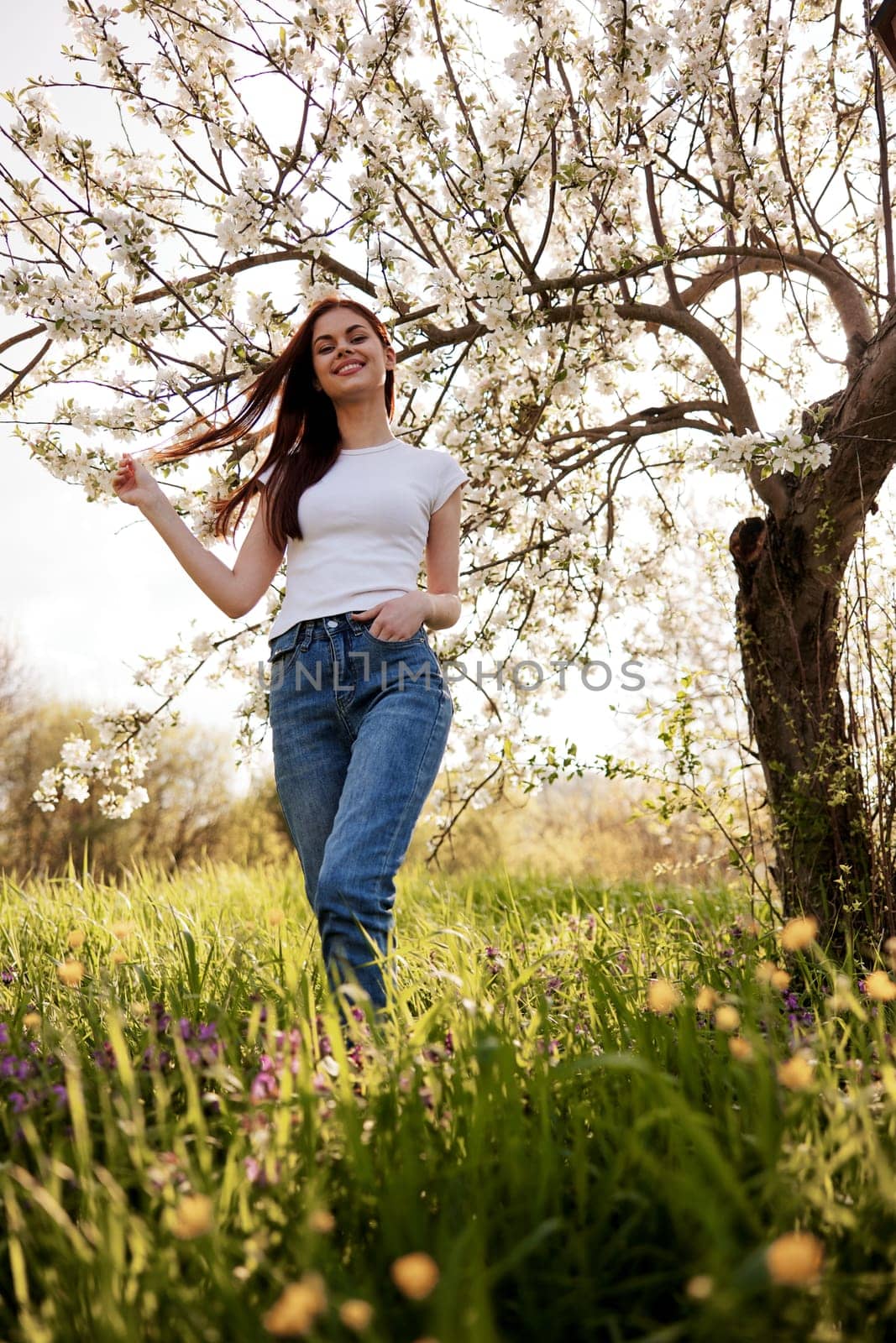 cheerful woman in casual clothes walks in nature near a flowering tree by Vichizh