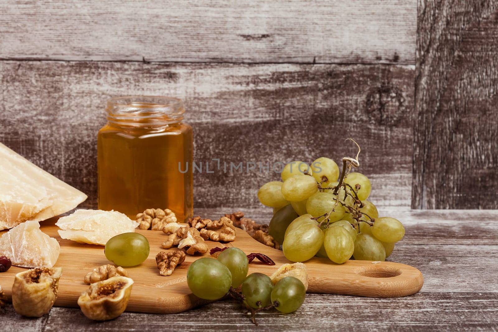 Parmesan, honey, nuts and grape on wooden background in studio photo. Healthy lifestyle