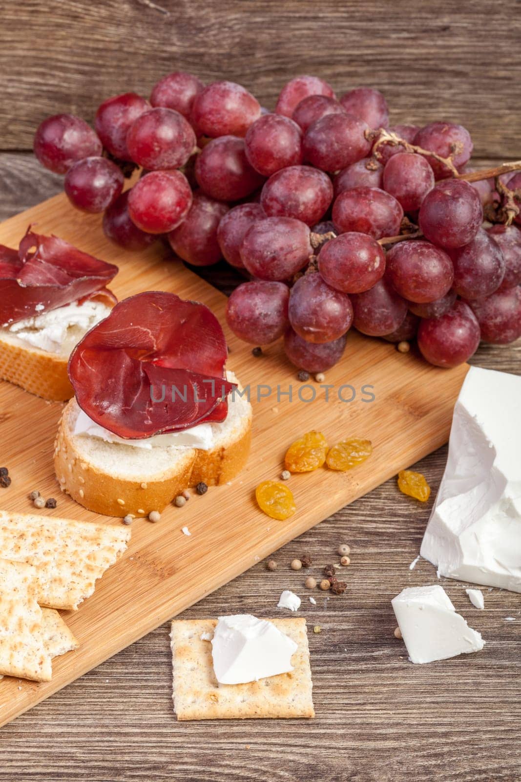White cheese, ham, crackers and grape on wooden background in studio photo. Healthy luxury lifestyle