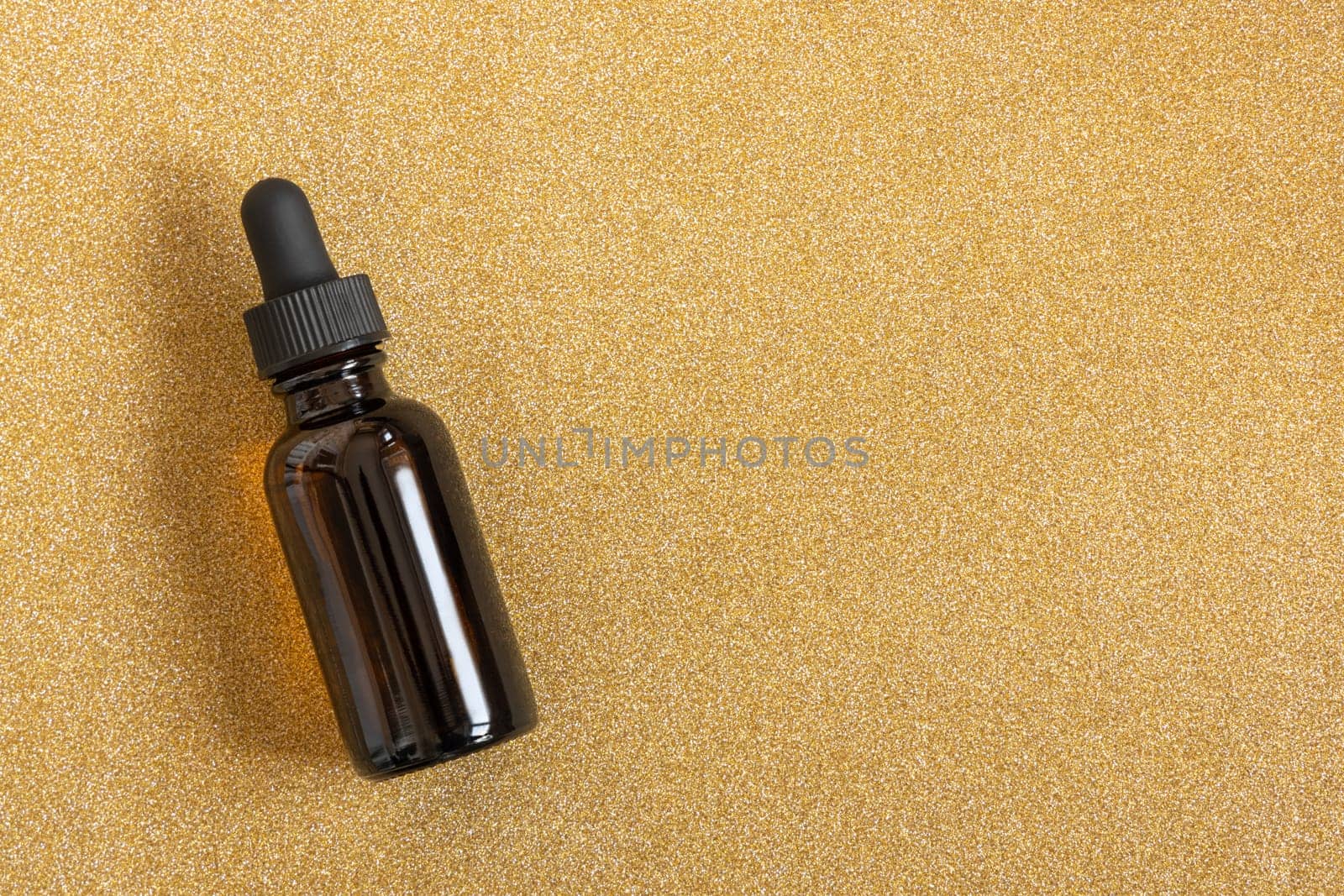 Cosmetic bottle dark glass with pipette on a golden shiny glitter background. Advertising mock up, copy space