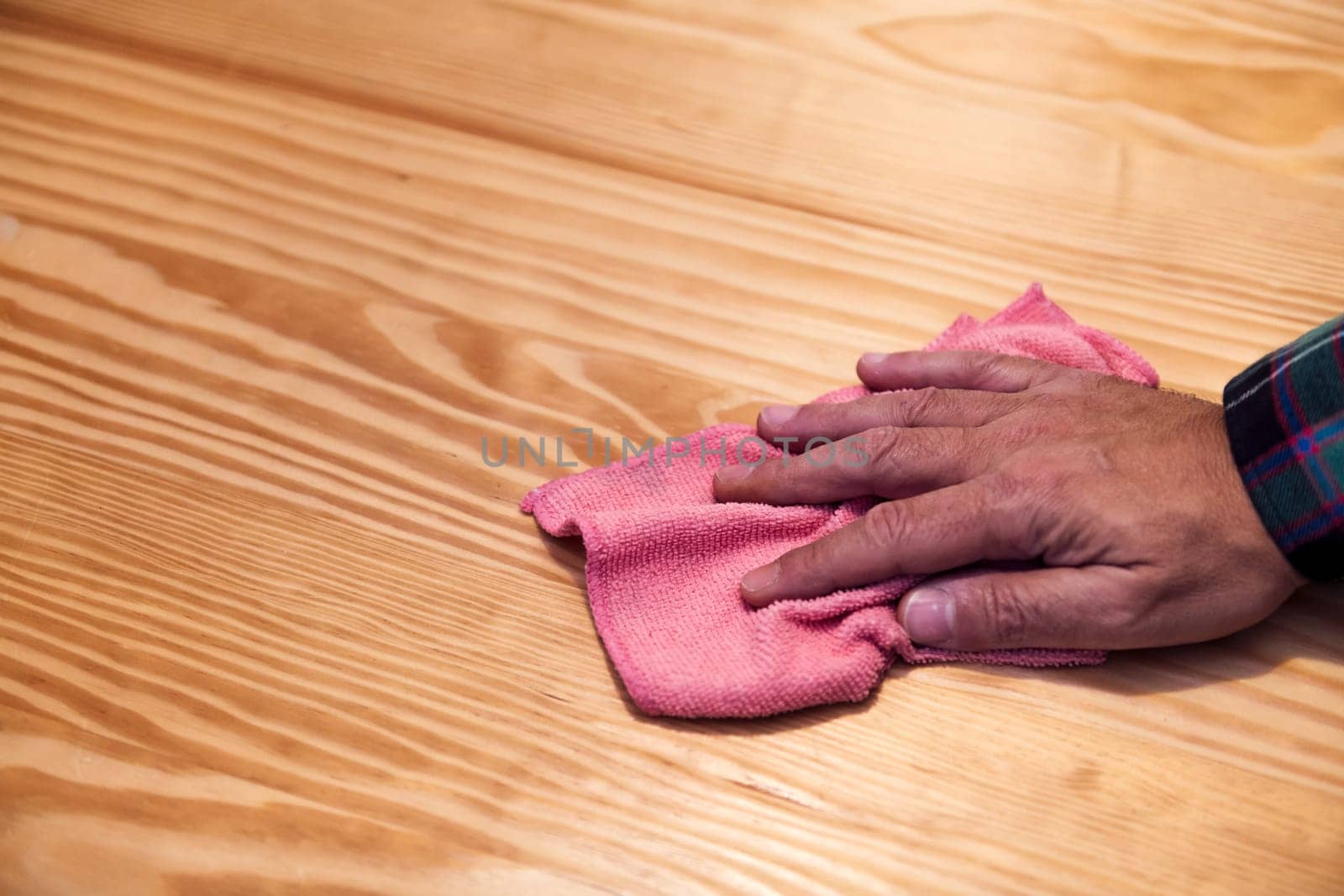 closeup of the hand of a person cleaning a wooden table with a rag, home cleaning concept, copy space for text