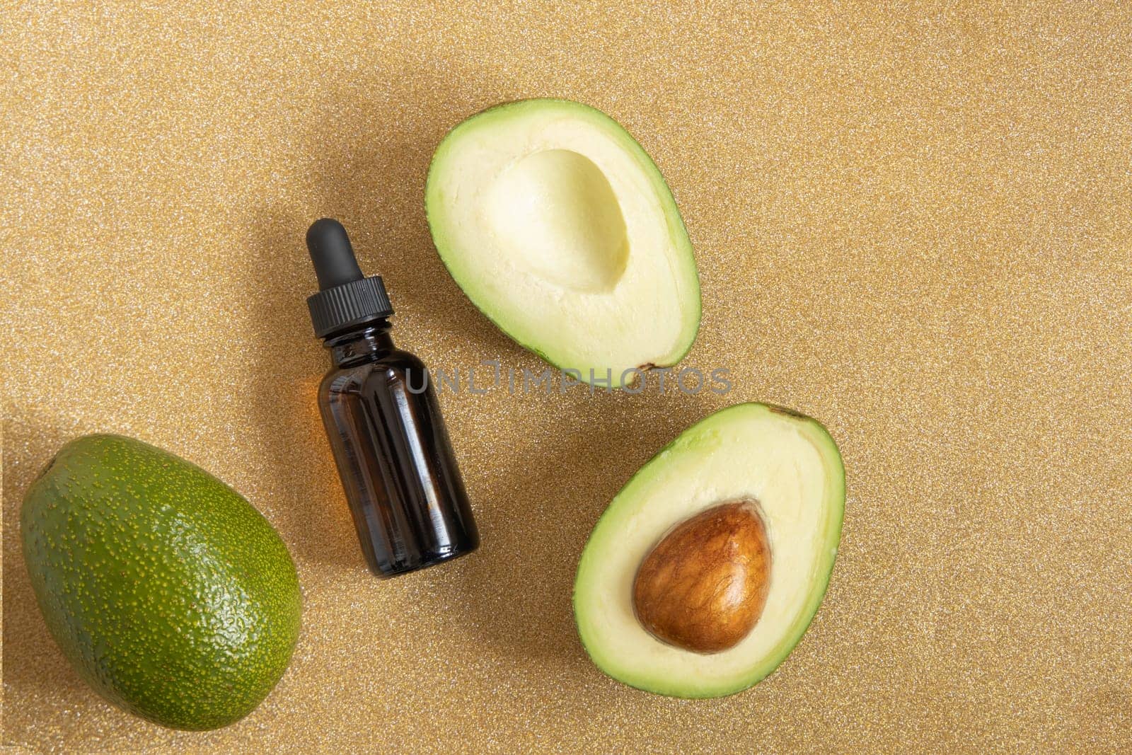 Avocado oil. Essential oil in dark glass bottle on shiny gold background. Avocado for healthy skin and hair. Cosmetics ingridient.