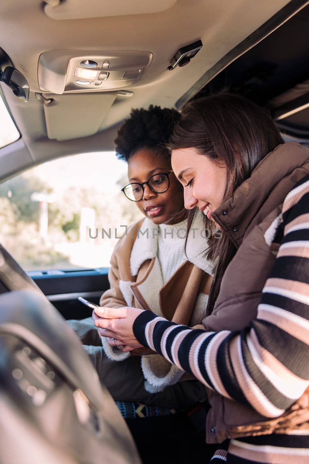 two young women in camper van checking road trip map on the phone, concept of adventure and travel with best friend