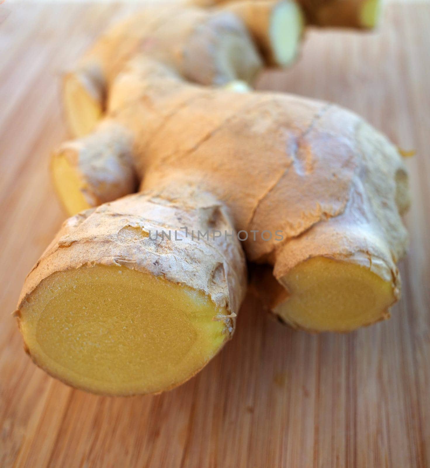 Part of an irregularly shaped fresh ginger root on a wooden cutting board